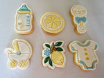 Load image into Gallery viewer, Six decorated sugar cookies shaped like baby items and a lemon motif, arranged on a light gray surface. The cookies are iced in white with pastel blue, yellow, green, and gold accents.
